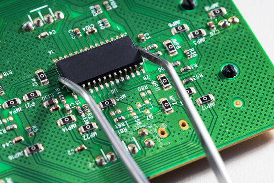 Tweezers holding a microchip processor on a green circuit board.