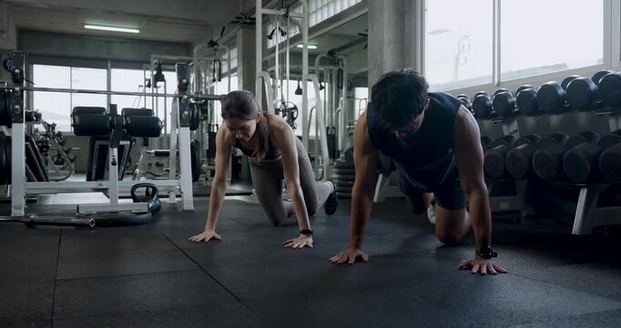 Young Asian couple performs push up exercise side by side on modern gym floor, moving through strength set together, building partner motivation, wellness, endurance, healthy couple teamwork routine