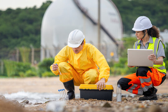 Environmental engineers team taking water samples for pollution testing at an industrial site, Professional scientists in safety gear analyzing water quality near an industrial plant