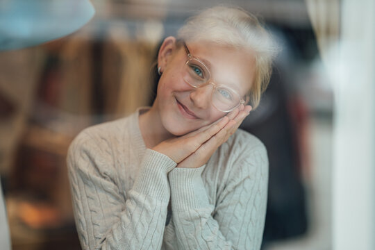 Happy child wearing stylish glasses standing inside a fashion store looking through the window at the vibrant street outside