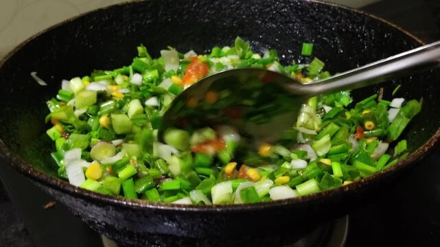 Close up of fresh green vegetables being stir-fried with tomatoes, lentils and traditional Indian spices in a pan, showcasing healthy vegetarian home cooking.