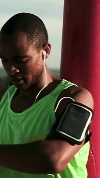 Vertical video: Checking wrist device, runner in neon tank adjusting black armband on boardwalk