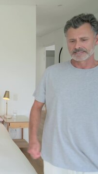 Vertical video: Adjusting mattress in bedroom, man gray tee white shorts spreading duvet making bed