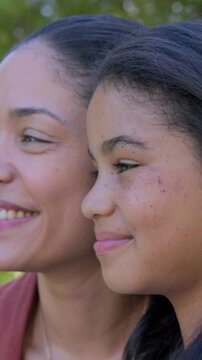 Vertical video: Moving mom near daughter, both turning and smiling in park with rust sleeve