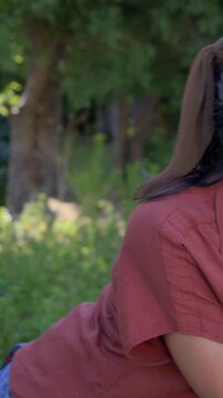 Vertical video: Pointing to cheek, woman laughing playfully and leaning to kid in park, rust shirt
