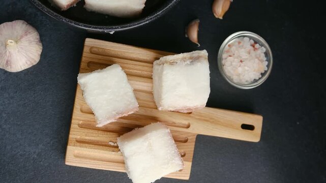 Raw cod pieces with salt and garlic on wooden board