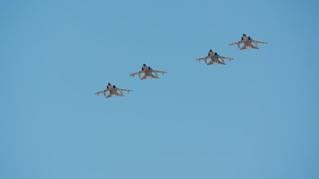Four fighter jets in slow motion flight, flying in diagonal formation across a clear blue sky, wings swept back, maintaining tight spacing and coordinated movement
