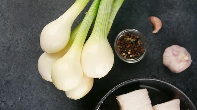 Green onions with garlic and peppercorns on a dark surface
