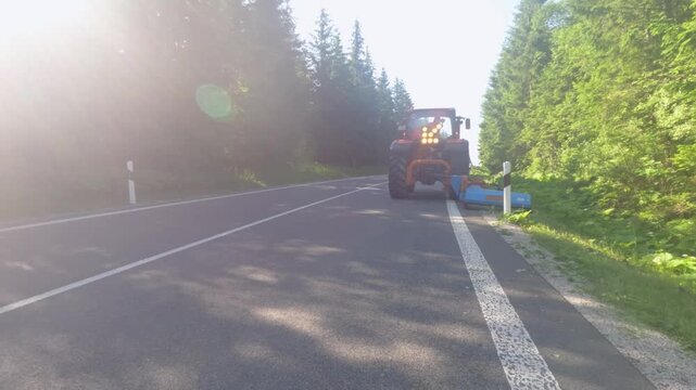 Agricultural tractor with a flail mower cutting grass and vegetation along a country road