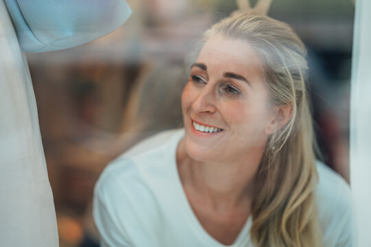 Beautiful blonde woman gazing through a boutique window creating a stylish portrait with reflections and elegant urban fashion atmosphere.