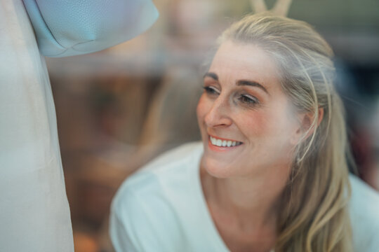 Portrait of a beautiful blonde woman looking through the fashion store window with an elegant expression in a modern urban shopping district.