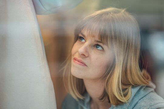 Beautiful blonde woman standing outside a fashion boutique looking through the display window in a stylish shopping district.