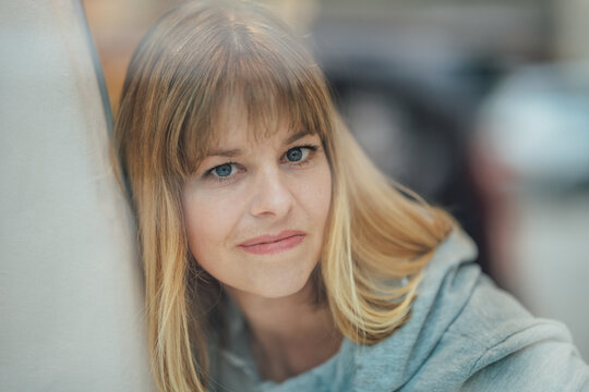 Elegant portrait of a blonde woman admiring a fashion store window with soft reflections and modern retail surroundings.