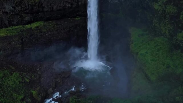 Solitary explorer standing on the edge of a rugged mountain cliff above a massive misty waterfall cinematic motion footage showing a person enjoying nature with arms raised high while surrounded by lu