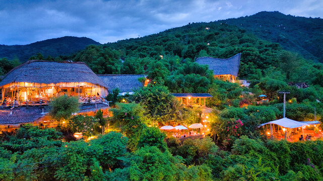 Aerial view of Jemeluk Beach Bungalows nestled in lush tropical greenery with illuminated thatched-roof structures and warm lighting at dusk in Kecamatan Abang, Bali, Indonesia.