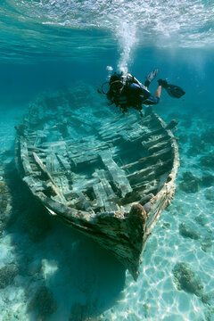 Scuba diver investigating clear tropical waters, above a shallow submerged vessel, using diving equipment and flippers