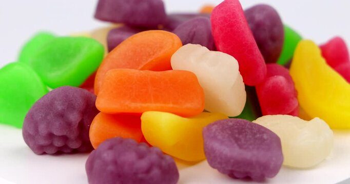 Close up spinning view of colorful fruit shaped candy candies on a round ceramic plate device layout over bright studio background