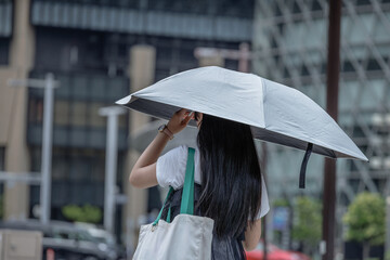 Rear view of woman holding a sun umbrella on a modern city street with contemporary architecture. © thomasgweber