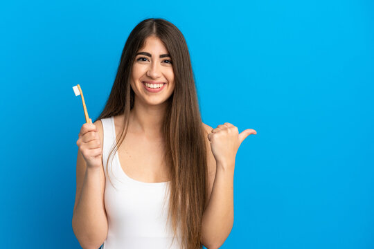 Young caucasian woman brushing teeth isolated on blue background pointing to the side to present a product