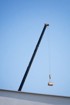 Black crane lifting a box container during construction work under clear blue sky
