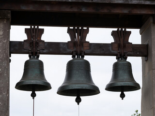 Obraz premium Three bronze bells hanging on a wooden frame against a cloudy sky