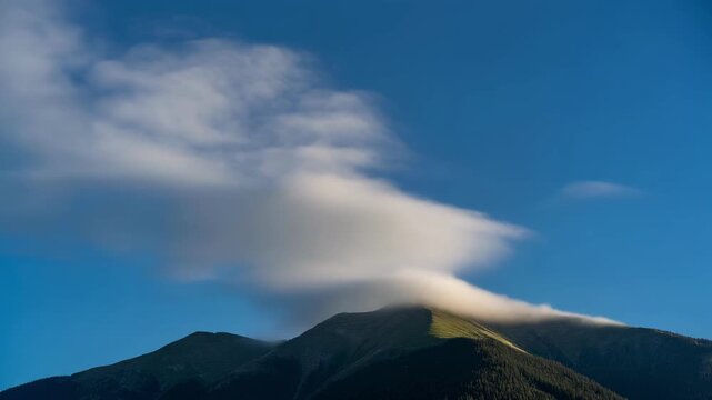 Wispy clouds drift over sunlit mountain peak under blue sky