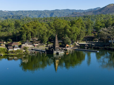 Aerial view of Pura Segara Ulun Danu Batur temple on the shore of Lake Batur, surrounded by lush green trees and mountains in Kecamatan Kintamani, Bali, Indonesia.