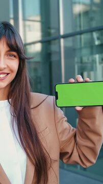 Confident businesswoman in suit smiling and holding a smartphone with a green screen. Perfect for showcasing mobile apps, user interface and UX designs, software demos, or tech startup presentations