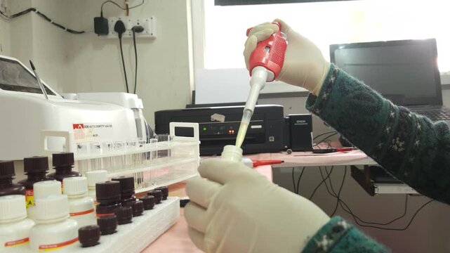 Laboratory technician preparing clinical samples with a micropipette, reagents, and test tubes beside an automated clinical chemistry analyzer. Ideal footage for healthcare, biotechnology, diagnostics