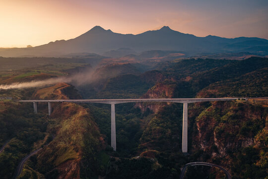Aerial view of Puente Beltran spanning a deep canyon with lush vegetation and winding roads below, set against a dramatic mountain backdrop in Tonila, Jalisco, Mexico.