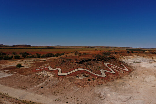 Aerial view of the Dreamtime Serpent land art installation winding across the red desert landscape near Birdsville, Queensland, Australia.