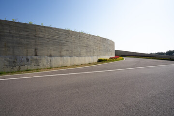 Obraz premium Curved asphalt road beside concrete retaining wall under bright sunlight
