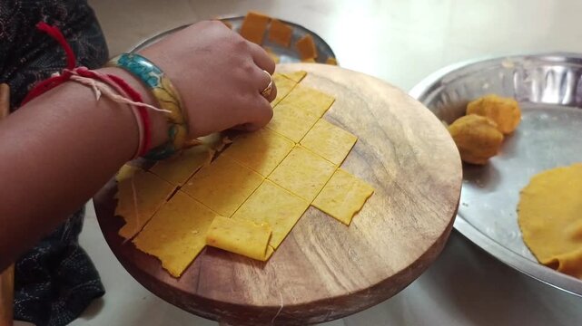 Indian Woman Hands Picking Diamond Shape Cut Yellow Dough Pieces from Wooden Board