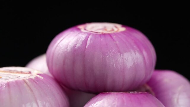 Pile of fresh peeled shallots slowly rotating on a black background.