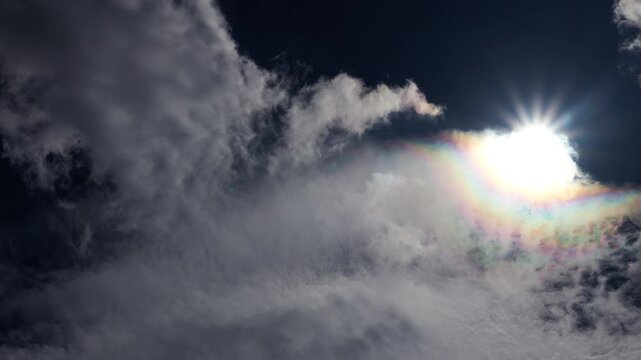 Real-time cloud iridescence transitioning to bright sunburst in deep blue sky.