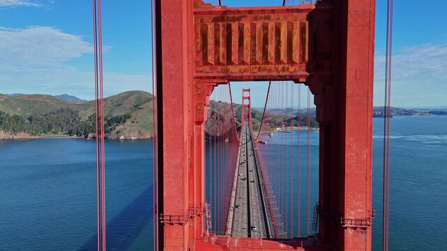 A high-angle, centered shot looking through the iconic red towers of the Golden Gate Bridge, showing the roadway and the surrounding bay waters.