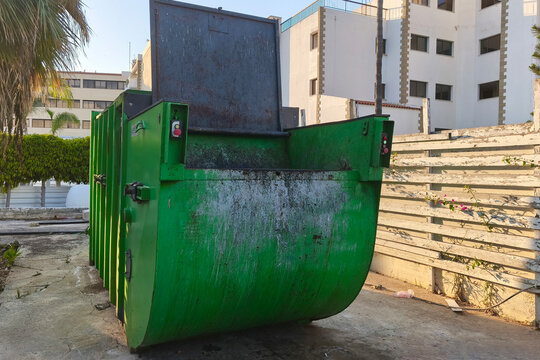 Industrial green waste compactor dumpster with an open lid in an urban service area, symbolizing waste management, recycling, sanitation, and environmental responsibility