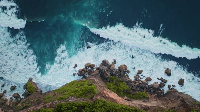 Ocean waves crashing onto the rugged coastline and rocky shore of the Bukit Peninsula, seen from an aerial bird's eye view high above the dramatic cliff in Uluwatu, Bali. Wild nature background
