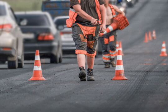 Road workers placing traffic cones during road repair on a busy city street, lane closure, asphalt resurfacing and traffic control