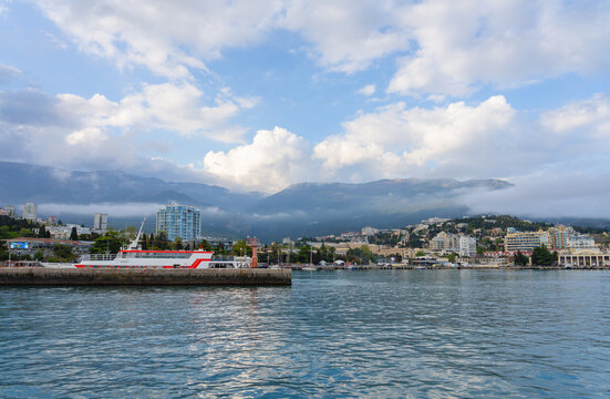 View of the Yalta embankment from the sea, mountains in clouds and a pier with a passenger ship