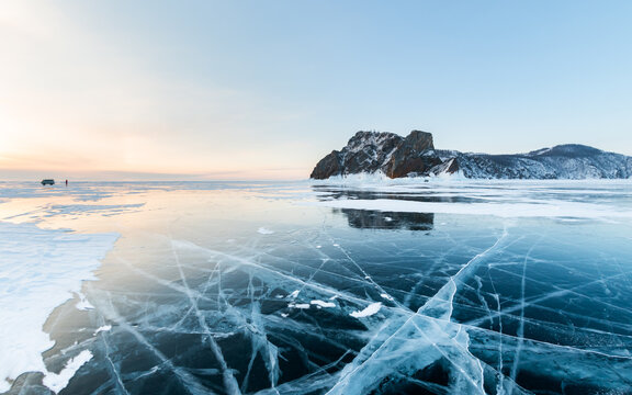 Blue transparent cracked ice with snow on Baikal lake in winter. Khoboy cape of Olkhon island, Baikal, Russia. Winter landscape at sunrise