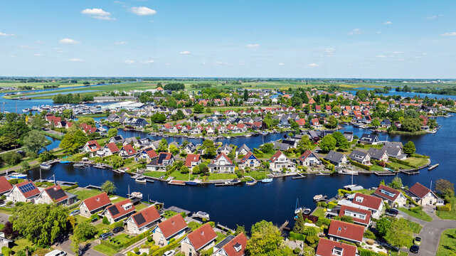 Aerial view of the village of Terherne with its characteristic houses, lush green gardens, and interconnected canals under a clear blue sky in Terherne, Friesland, Netherlands.