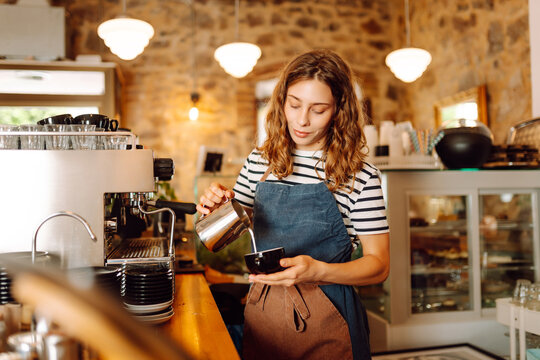 Female barista prepares aromatic coffee standing at bar near coffee machine. Woman works in coffee shop and enjoys fresh coffee indoors. Concept of drinks, coffee shops, employees.