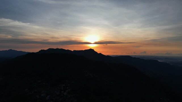 Mountain sunrise, golden sun behind peak, orange sky clouds, misty valley, dark silhouette landscape, cinematic aerial drone footage, nature background, travel scenery | Haputale, Sri Lanka