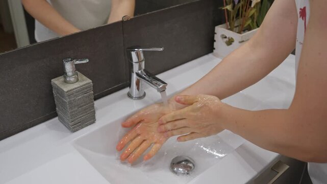 Person washing hands with soap in bathroom sink