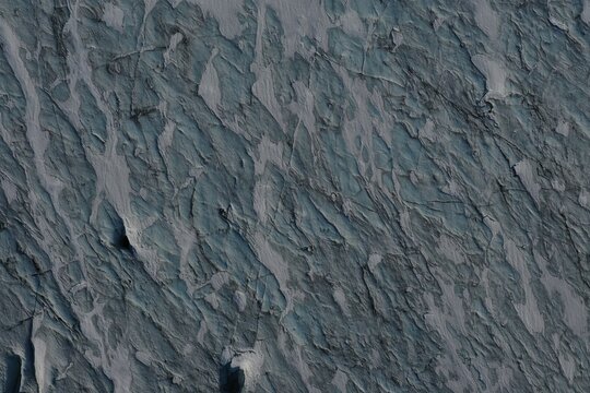 Aerial view of the textured surface of a glacier with deep blue crevasses and intricate ice patterns in Vik, Myrdalshreppur, Iceland.