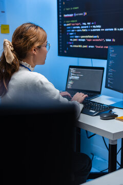 Concentrated Asian Female Software Developer, Programmer using Desktop computer, Writing code, Developing Software Working on Ai Machine learning project sits at office desk in tech office at night.