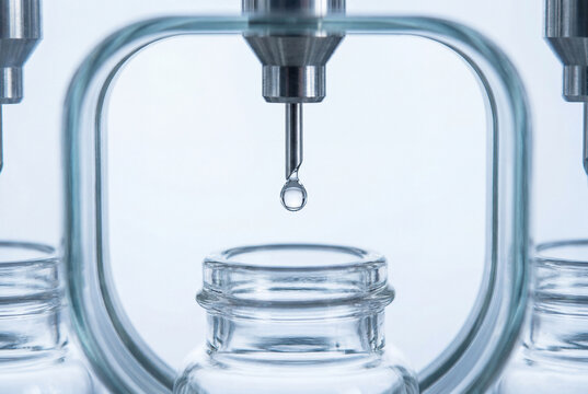 Pharmaceutical dispensing nozzle above sterile glass vial before filling