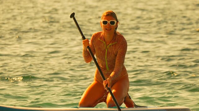 Paddleboarding woman ocean kneeling paddleboarder enjoying fitness exercise during golden hour sunset