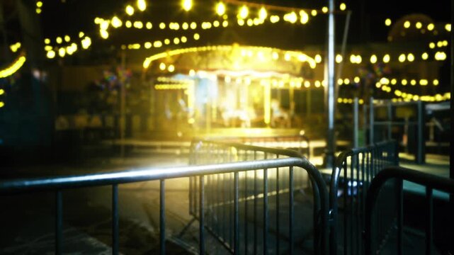Closed fairground gate with glowing carousel, metal railings in foreground, carousel lights haloed in background, wet surfaces reflecting amber bulbs, empty